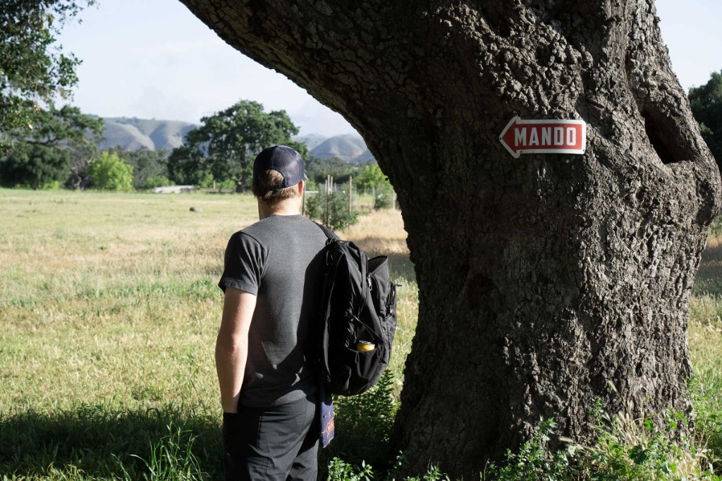 A disc golfer standing beside a tree with a mando sign
